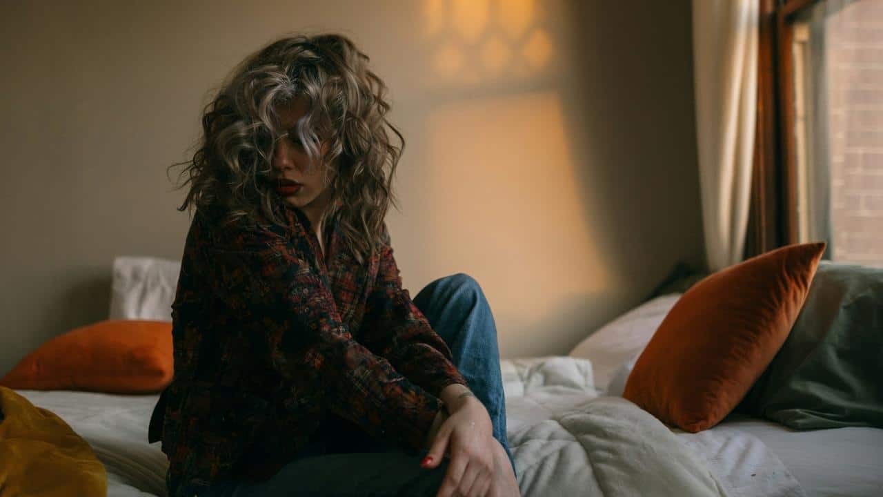 A woman sits on a bed in a dimly lit room.