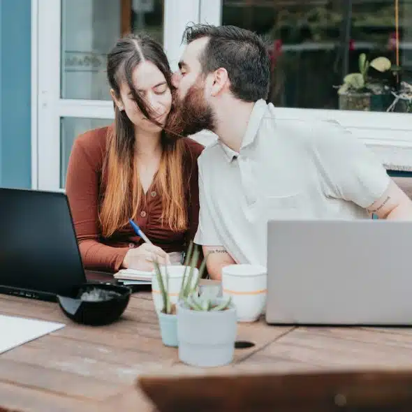 A man and woman kissing in front of a laptop