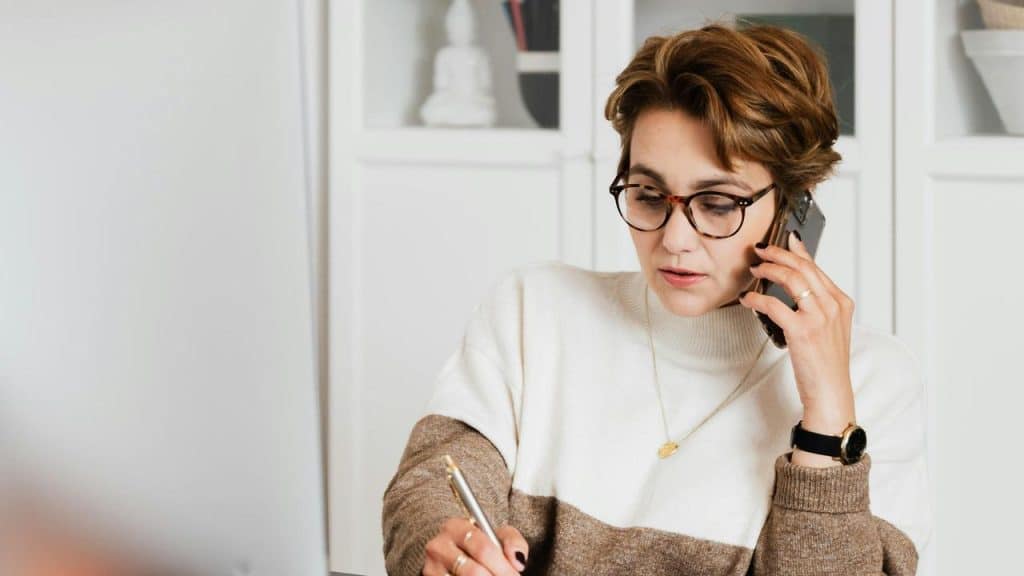 A woman talking on the phone while writing at her desk.