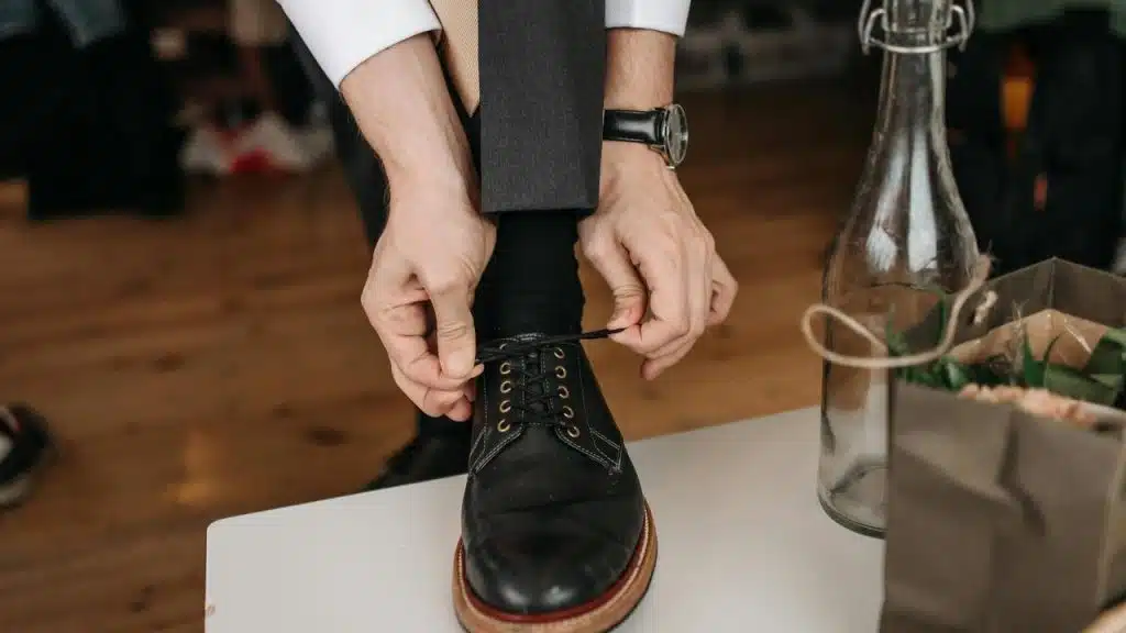 A person tying the laces of a black dress shoe.