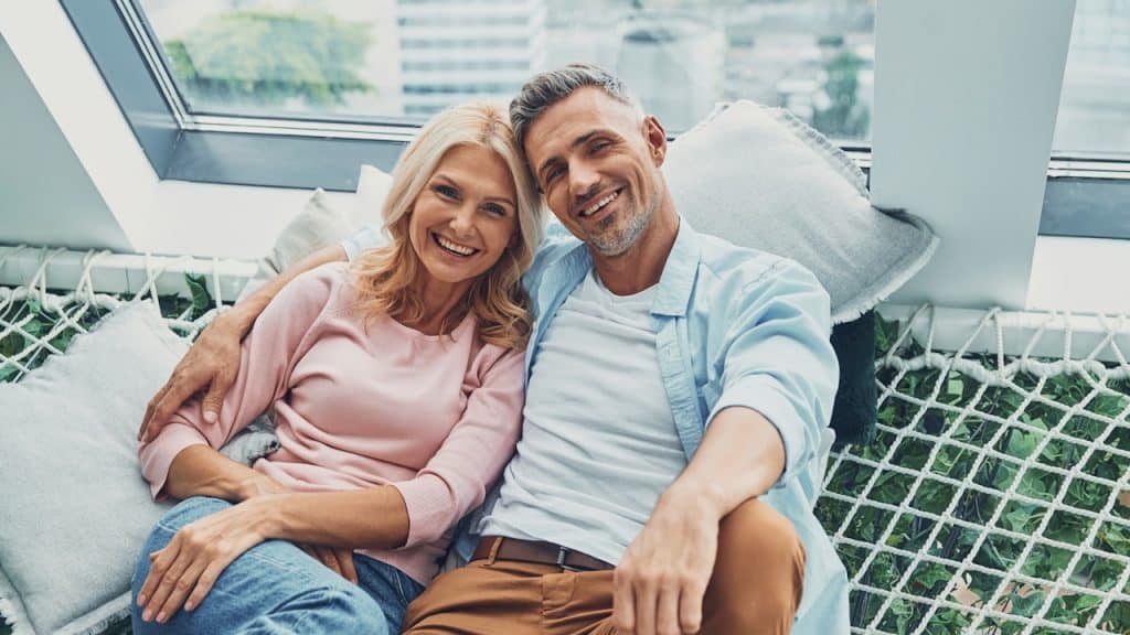 A happy mature couple smiling and looking at the camera while relaxing in a big hammock at home together.