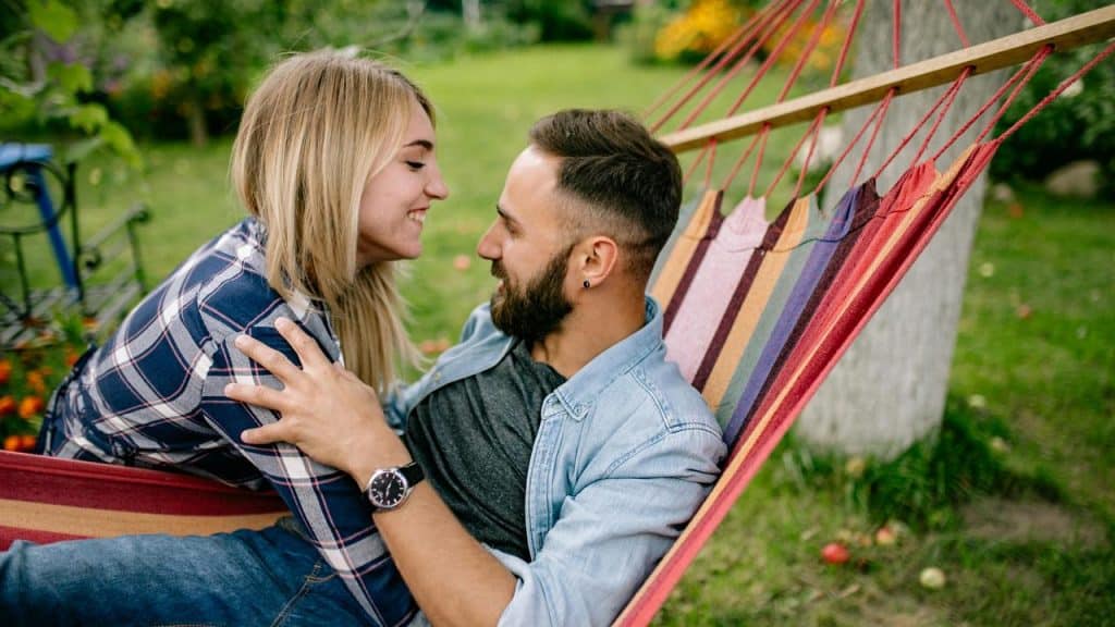 A smiling couple relaxing together on a hammock outdoors.
