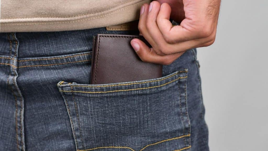 A hand placing a brown wallet into a back pocket.