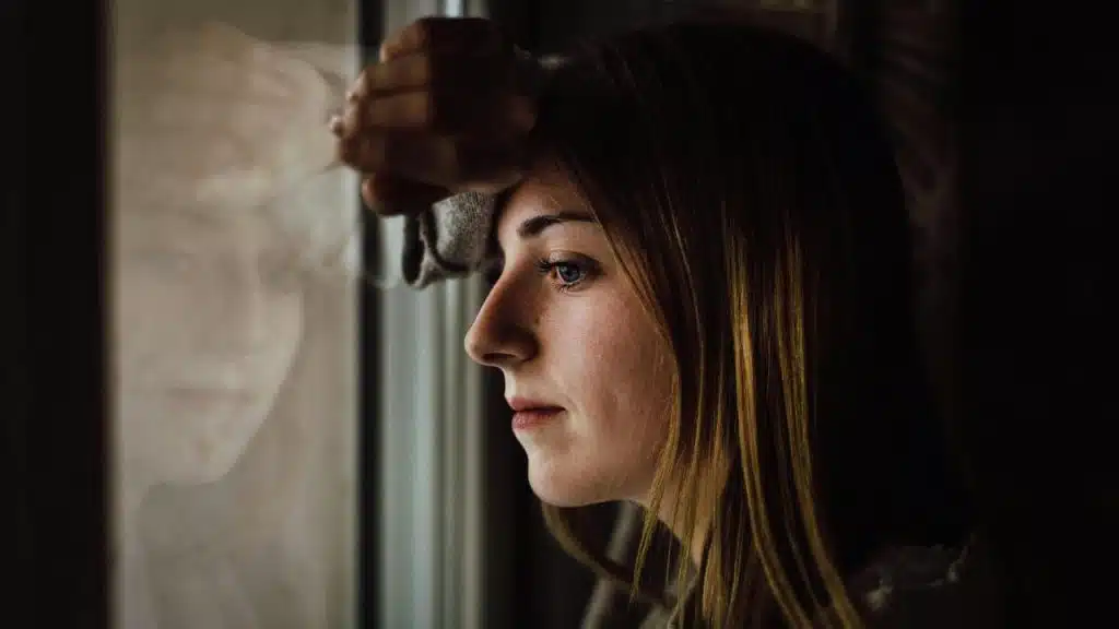 A woman leaning on a window frame looking outside thoughtfully.