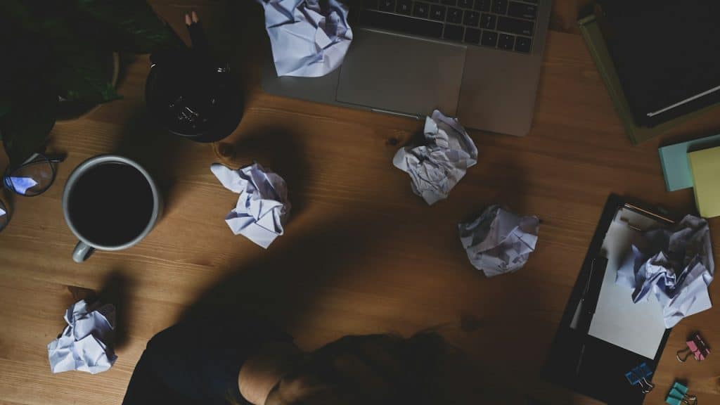 A stressed man surrounded by crumpled papers.