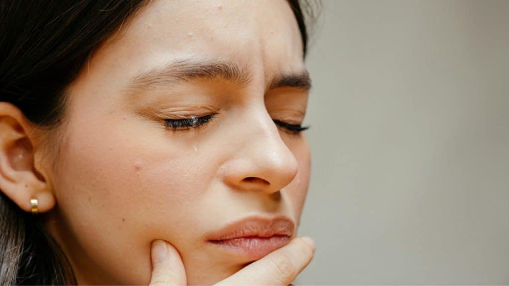 Close-up of a woman with closed eyes and a tear, holding her chin.