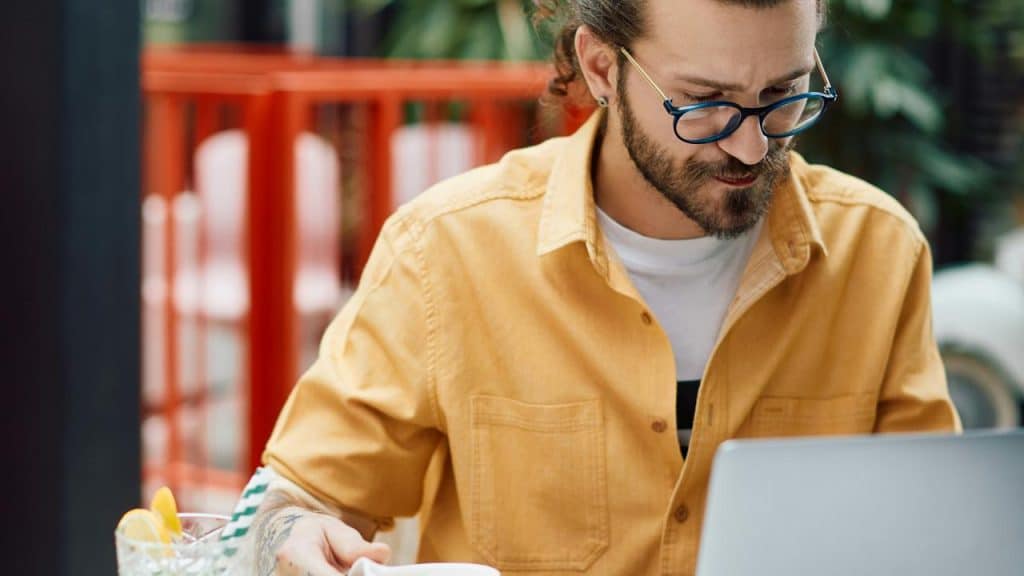 A man in glasses working on a laptop while holding a cup.