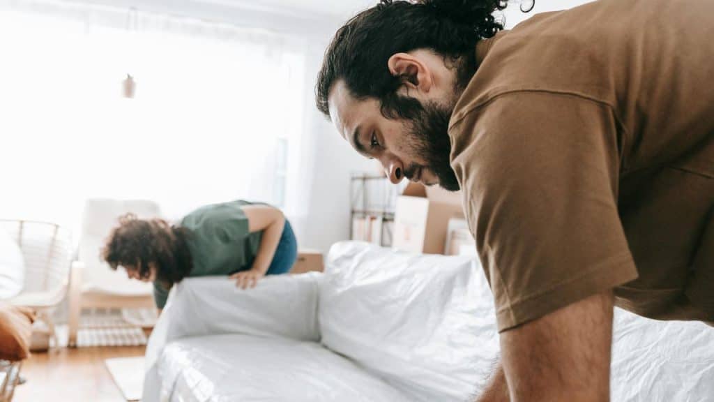 A man and woman setting up or moving a couch in a bright room.