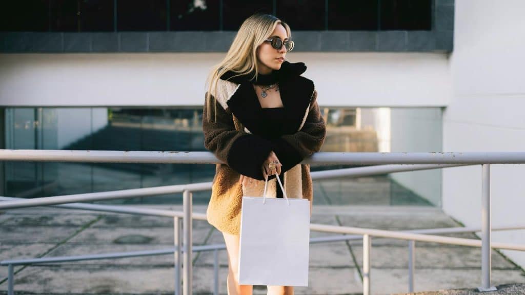 Woman in stylish coat holding shopping bag outdoors