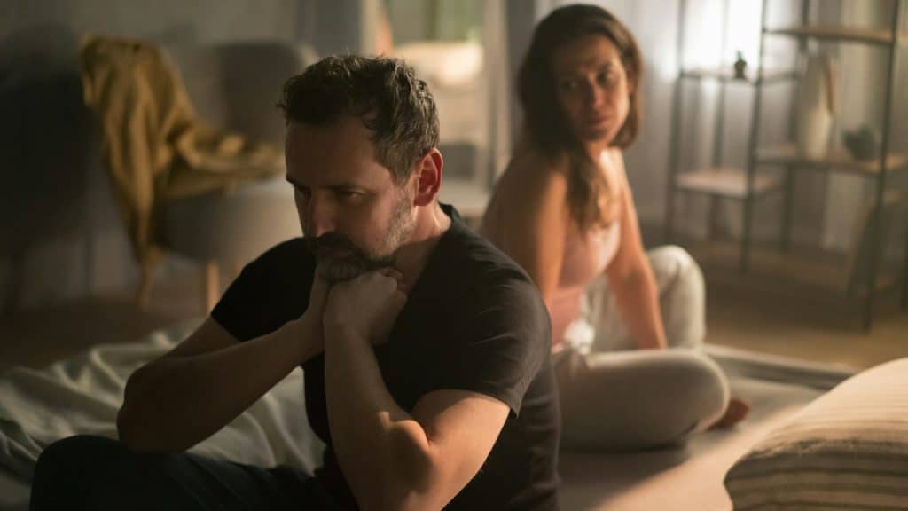 A lightly bearded man with his back to a woman and looking depressed.