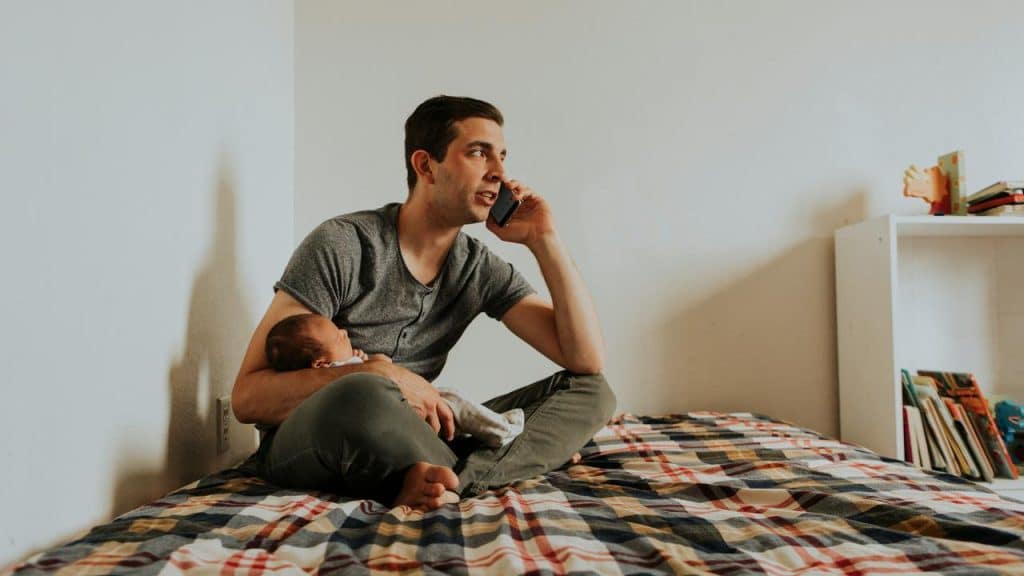 A man calling on the phone while cradling a baby with one arm.