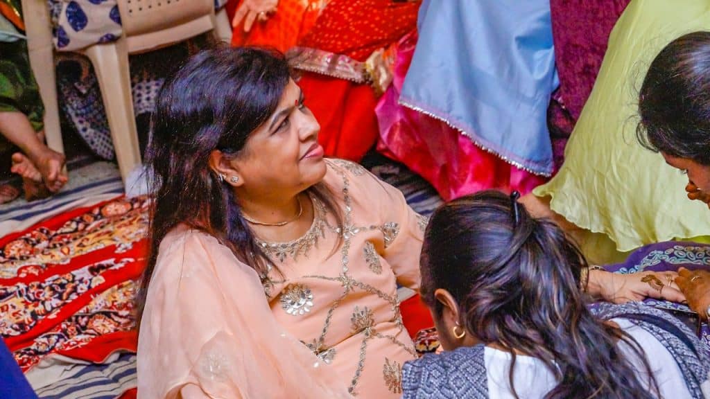 Two girls applying henna to an elderly lady who is getting ready for a marriage function in India.