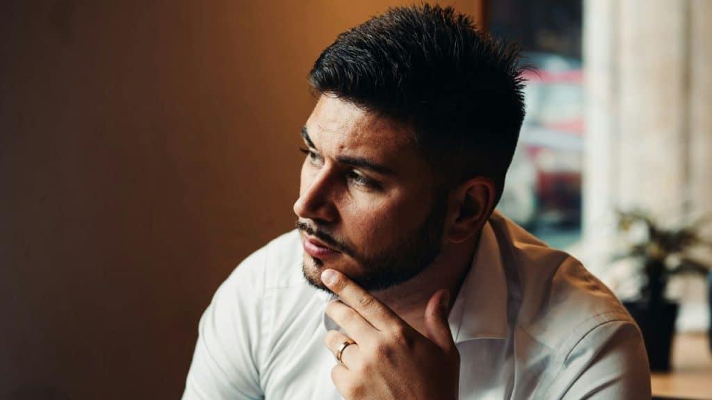 Portrait of a thoughtful man in a white shirt, hand on chin, looking away.