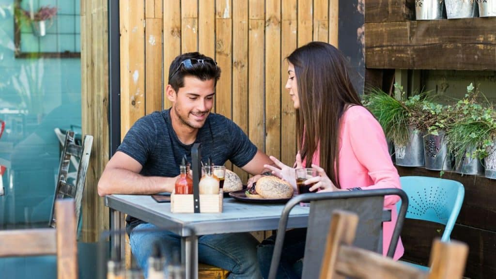 A happy man and woman are talking and eating at an outdoor cafe table.