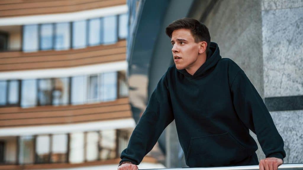 A man in a black hoodie leaning on a railing outdoors.