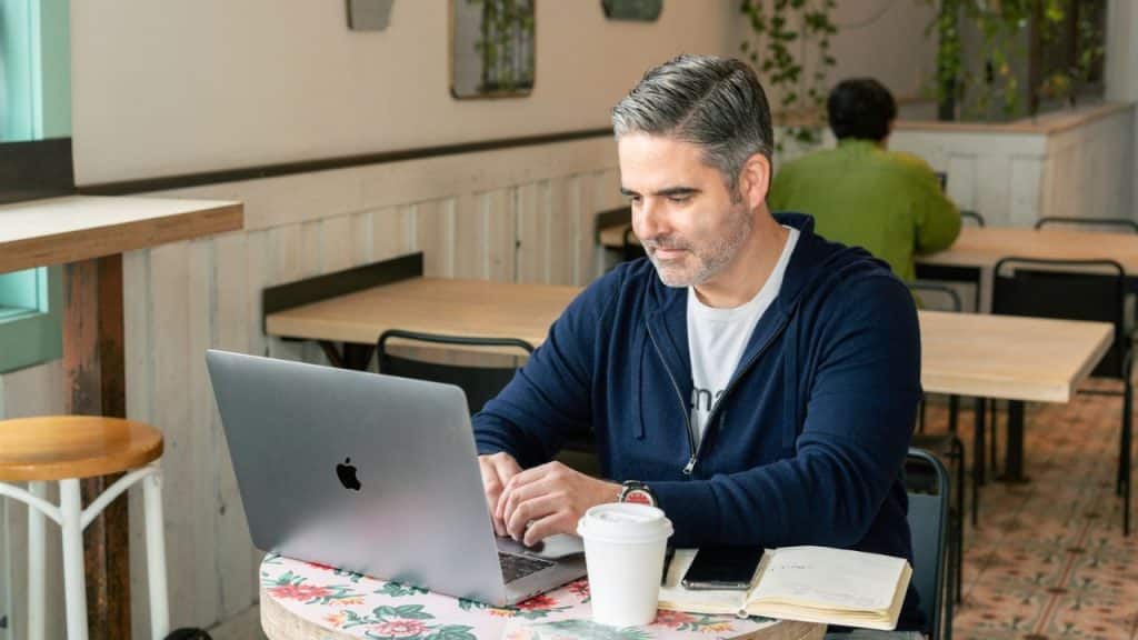 A focused man working on a laptop at a small patterned table in a cafe.