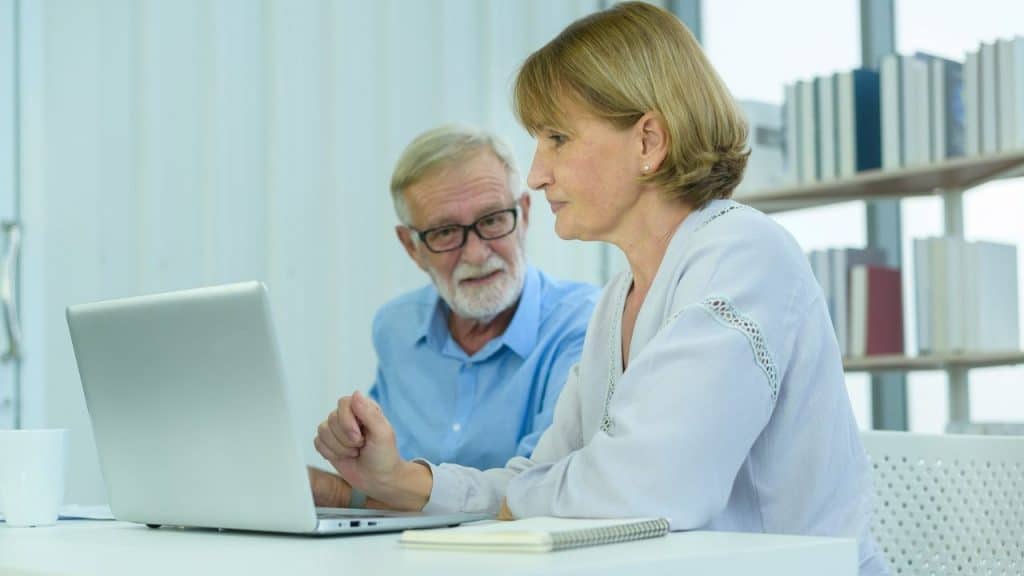 Mature woman pointing at a laptop screen while a man watches her.