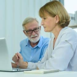 Mature woman pointing at a laptop screen while a man watches her.