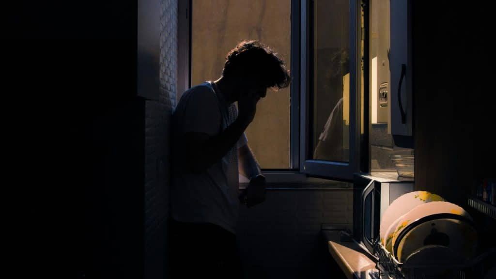 A man standing in a dimly lit kitchen near a window.