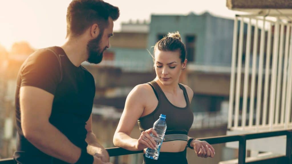 Man and woman in athletic wear on a balcony, the woman holding a water bottle.