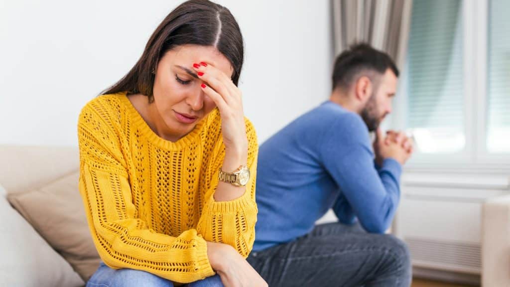 Unhappy, thoughtful, married couple spouses sitting separately on a couch.