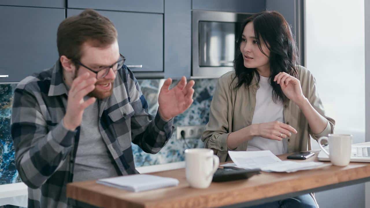 A man and woman with their hands up and arguing at each other.