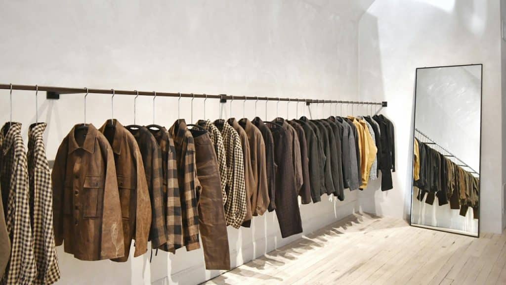 A room with a wall with a rod and male clothes hanging on it.