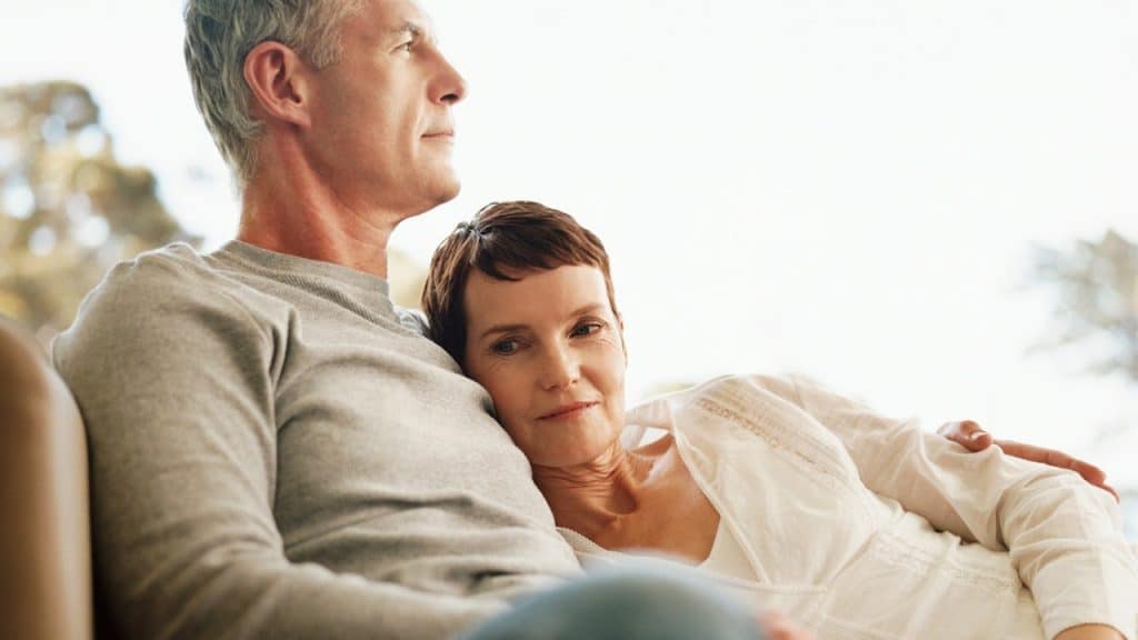 An elderly woman lying on the shoulders of her husband.