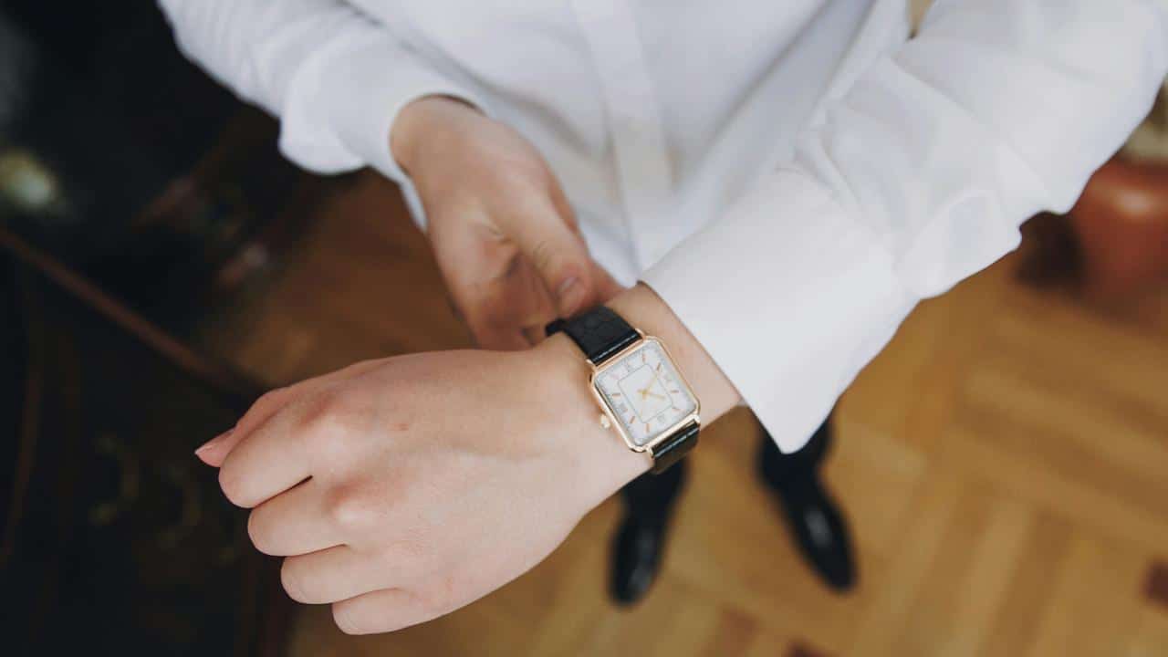 A person in a white dress shirt adjusts a wristwatch on their left hand.
