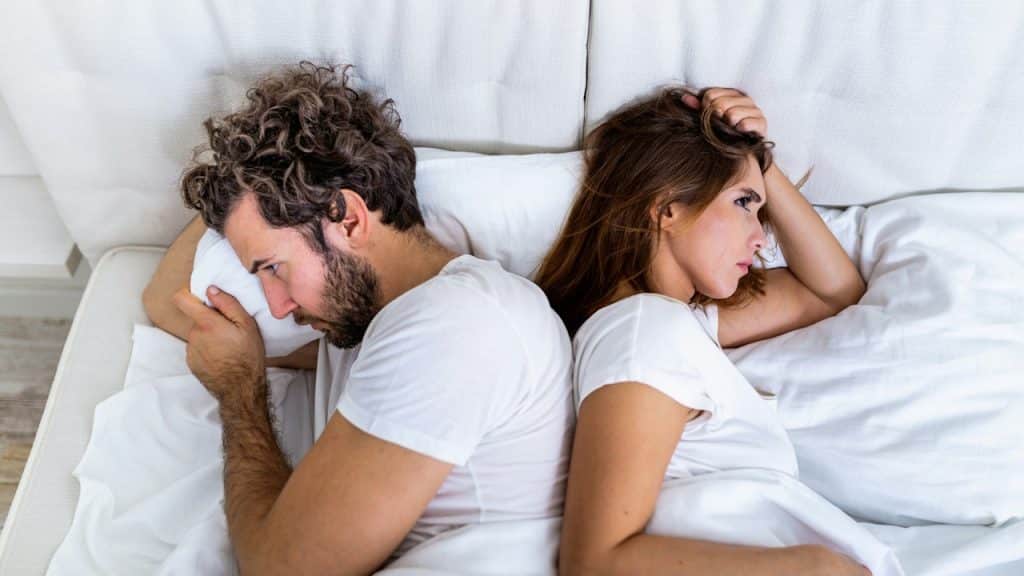 Couple lying in bed back-to-back, seemingly angry or upset after an argument.