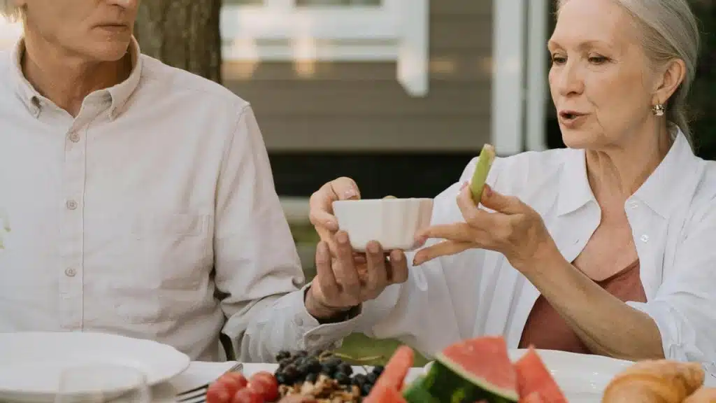 An elderly couple sitting outdoors at a table sharing food together.