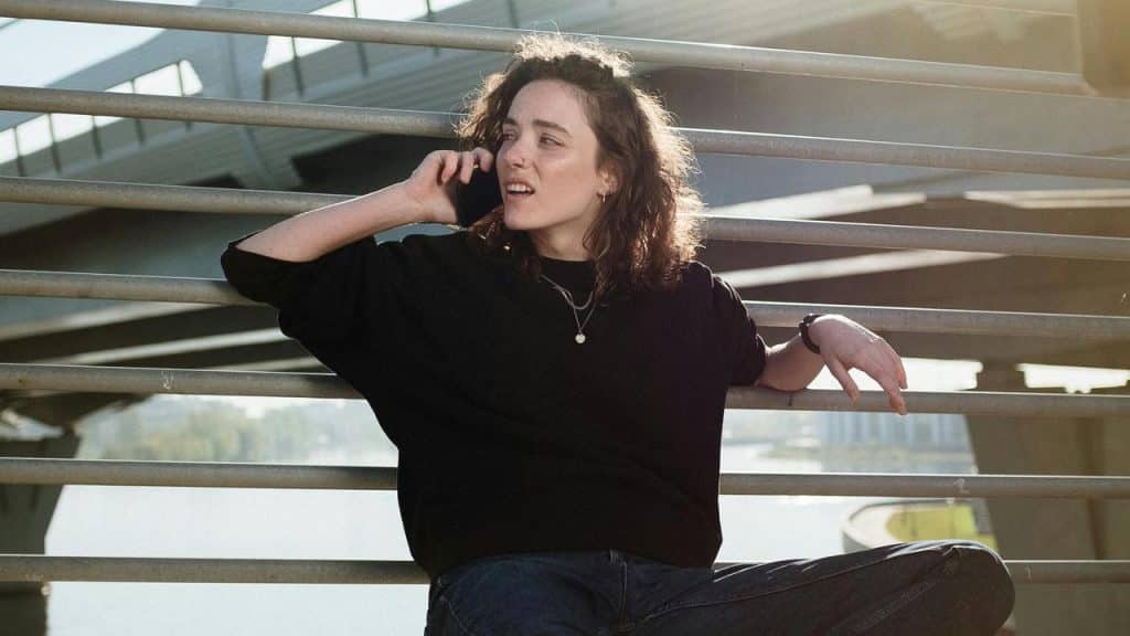 A woman sitting outdoors against metal railings while talking on her phone.