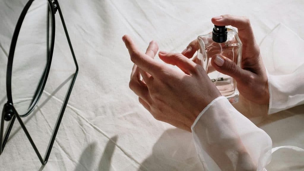 An elegant hand holding a perfume bottle near a small mirror.