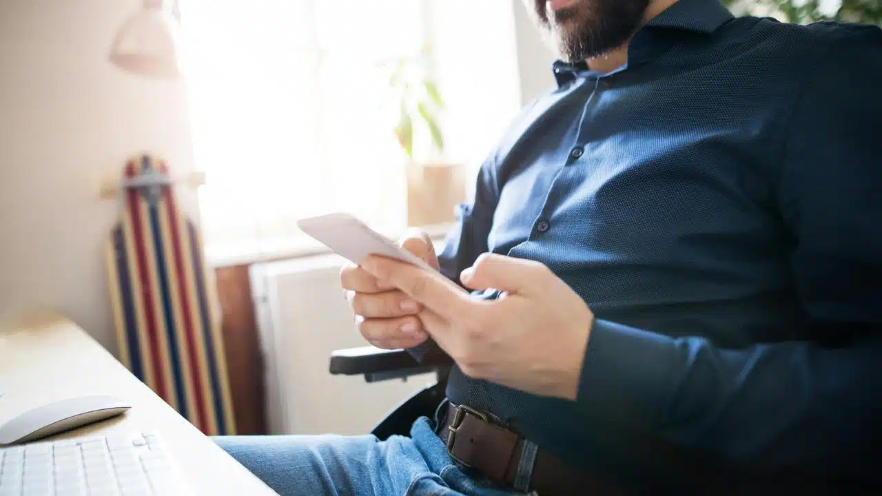 A man sitting at a desk using a smartphone.