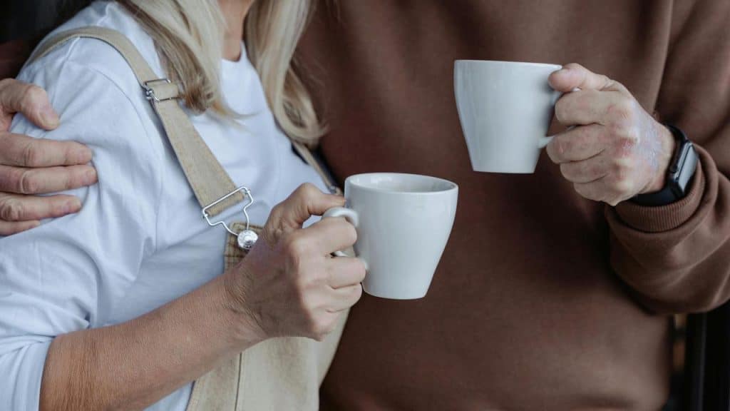 A close-up of a couple holding white mugs together.
