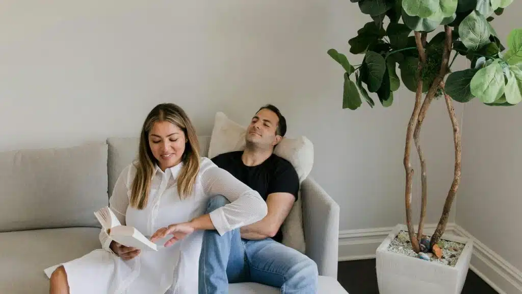 A woman reading a book while a man relaxes beside her on a couch.