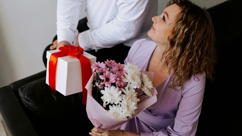 A man giving a present and a bouquet of flowers to his wife.