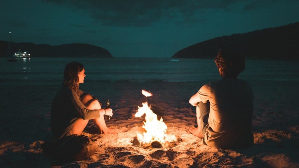 A couple sitting by a fire on a beach.