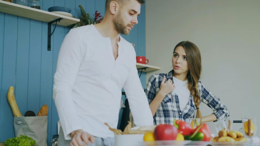 A woman speaks animatedly to a man who appears disinterested in a kitchen.