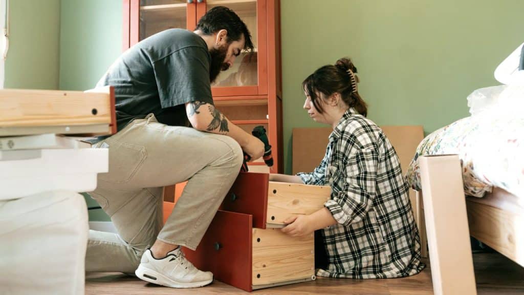 A man and a woman work together to assemble wooden furniture in a room.