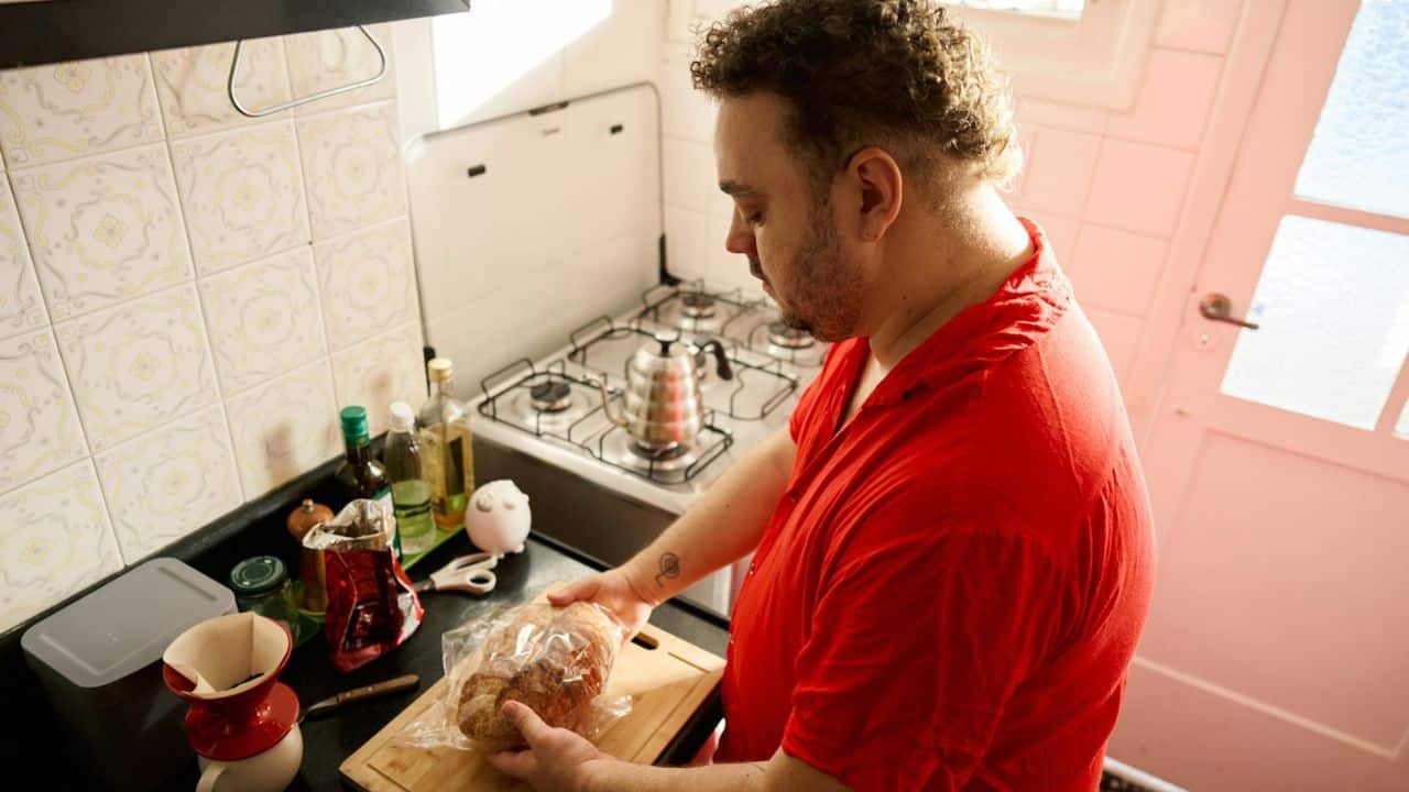 A man in a red shirt holds a packaged loaf of bread in a kitchen.