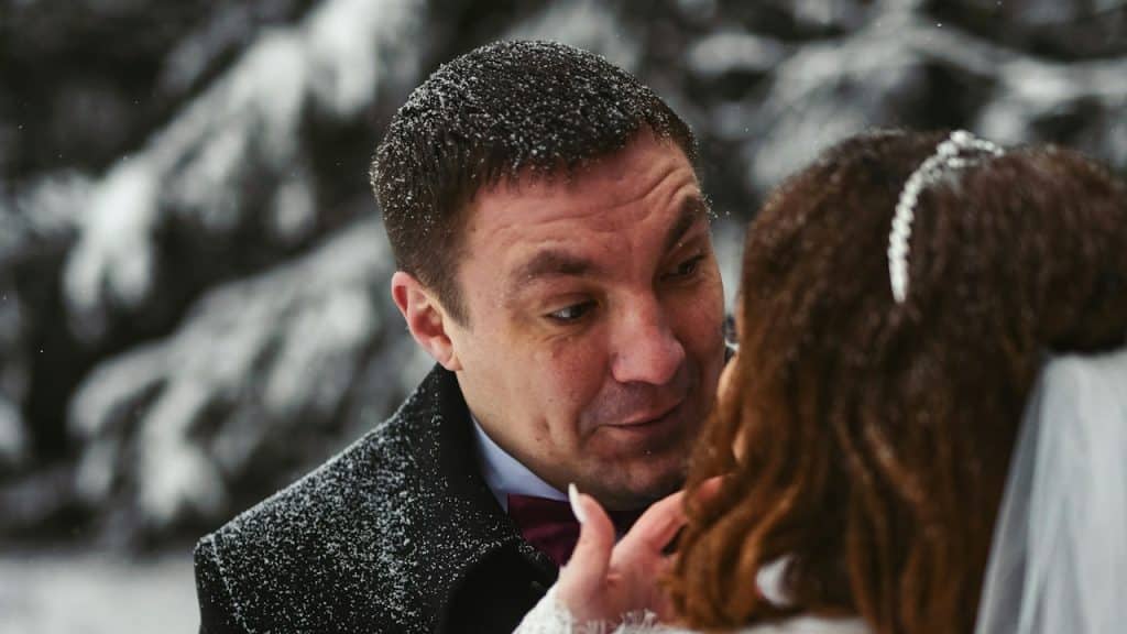 A man touches a woman’s face gently while standing in snow.