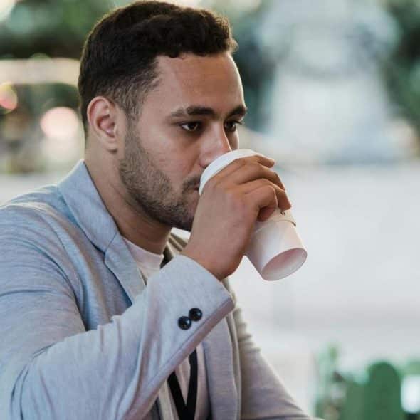 A man in a light jacket drinking from a paper cup.