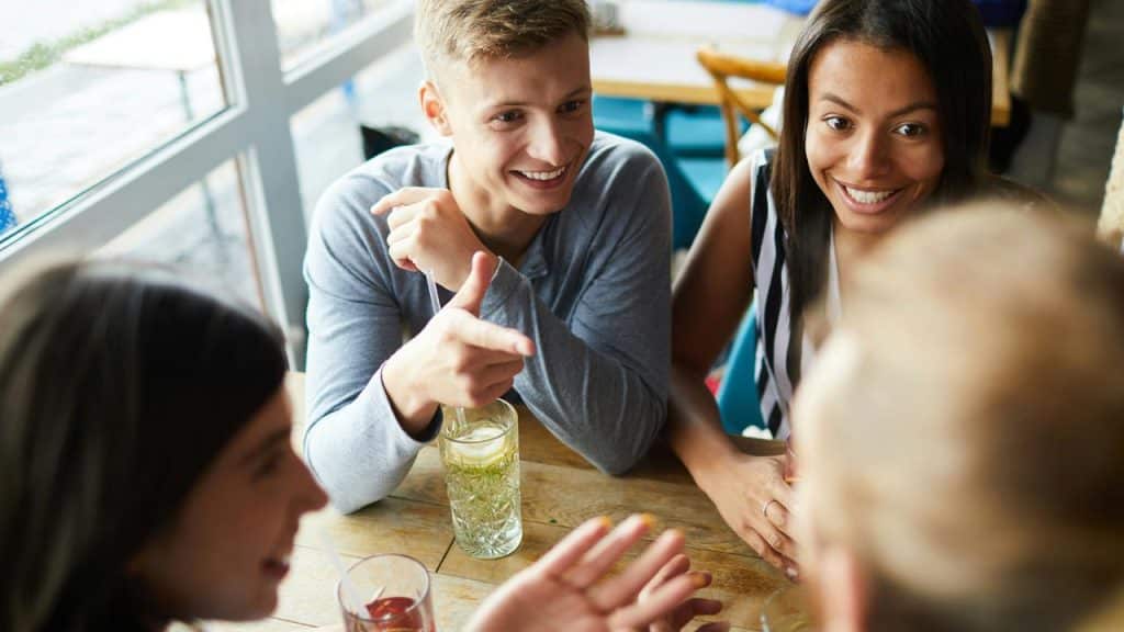 An excited group of friends smiling and talking around a café table.