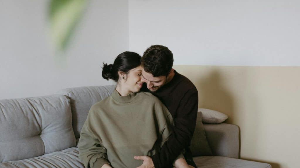 A couple sitting closely on a couch, leaning their foreheads together affectionately.