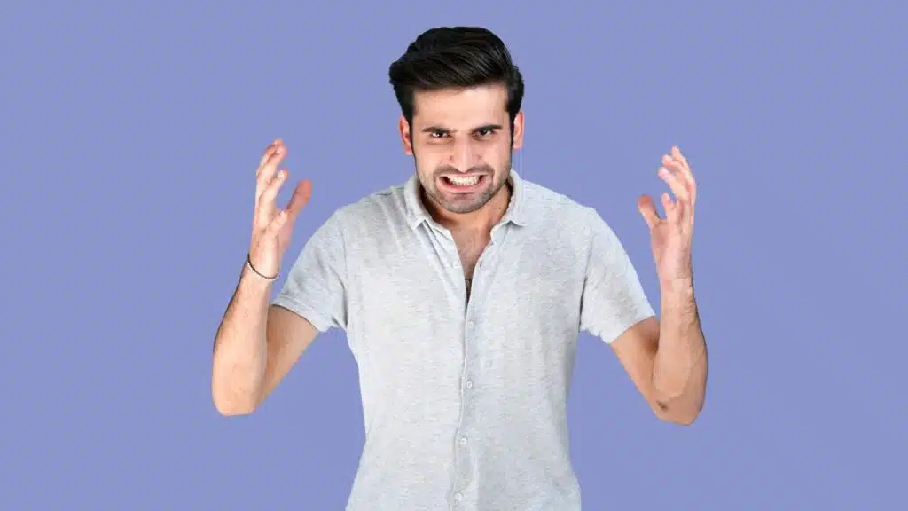 A man with a fierce expression is clenching his teeth and holding up his hands.