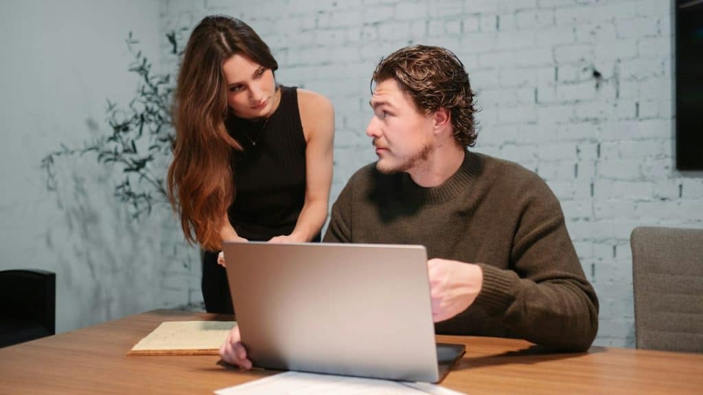 A man and woman looking at a laptop together at a wooden desk.