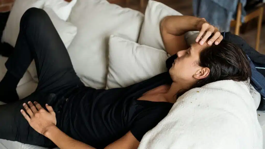A man is lying on a couch with his hand resting on his forehead.
