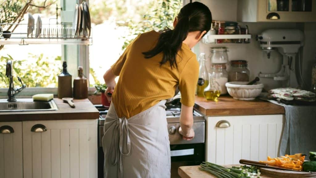 Woman in a yellow shirt and apron cooking in a bright kitchen.