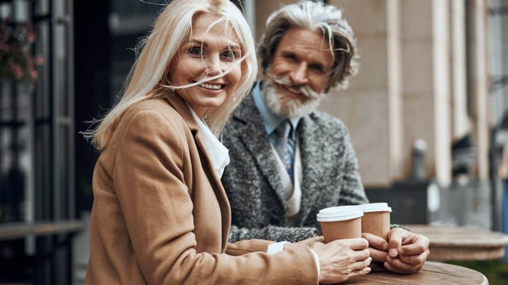 A gladsome woman turned and smiled while sitting with a man at the cafe table.